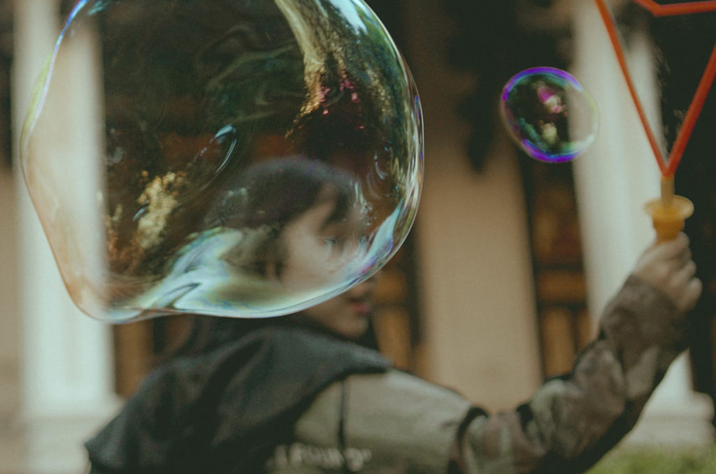 Uma bolha de sabão colorida cobre o rosto de uma criança. Imagem que ilustra o papel do lazer no processo de desenvolvimento pessoal.