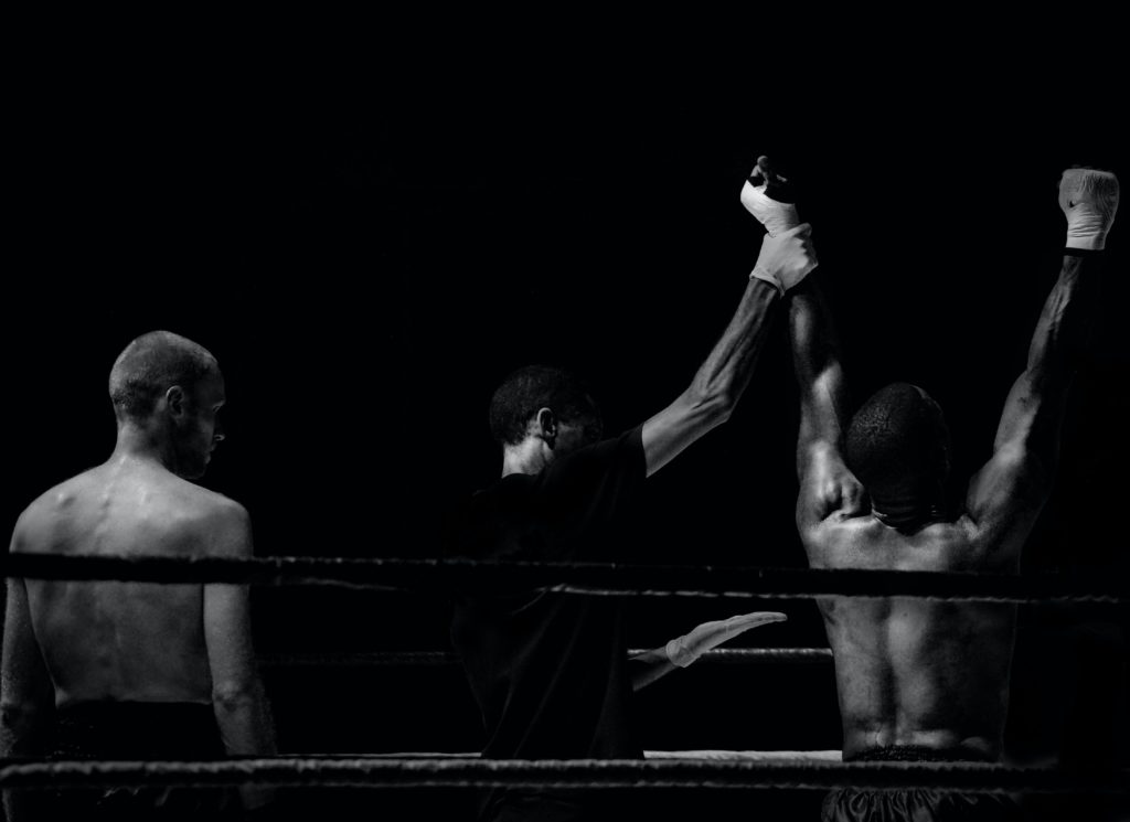 Foto preto e branca num ringue de box com um juiz levantando a mão do vencedor