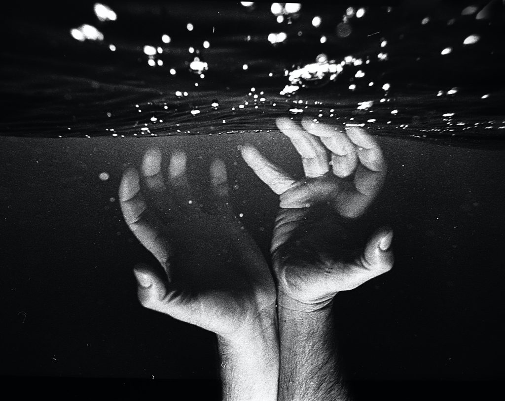 foto preto e branca com duas mãos mergulhando na água simulando certo desconforto.