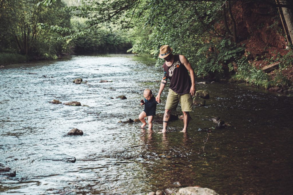 Um homem branco com criança pequena atravessando um rio numa relação de parentalidade